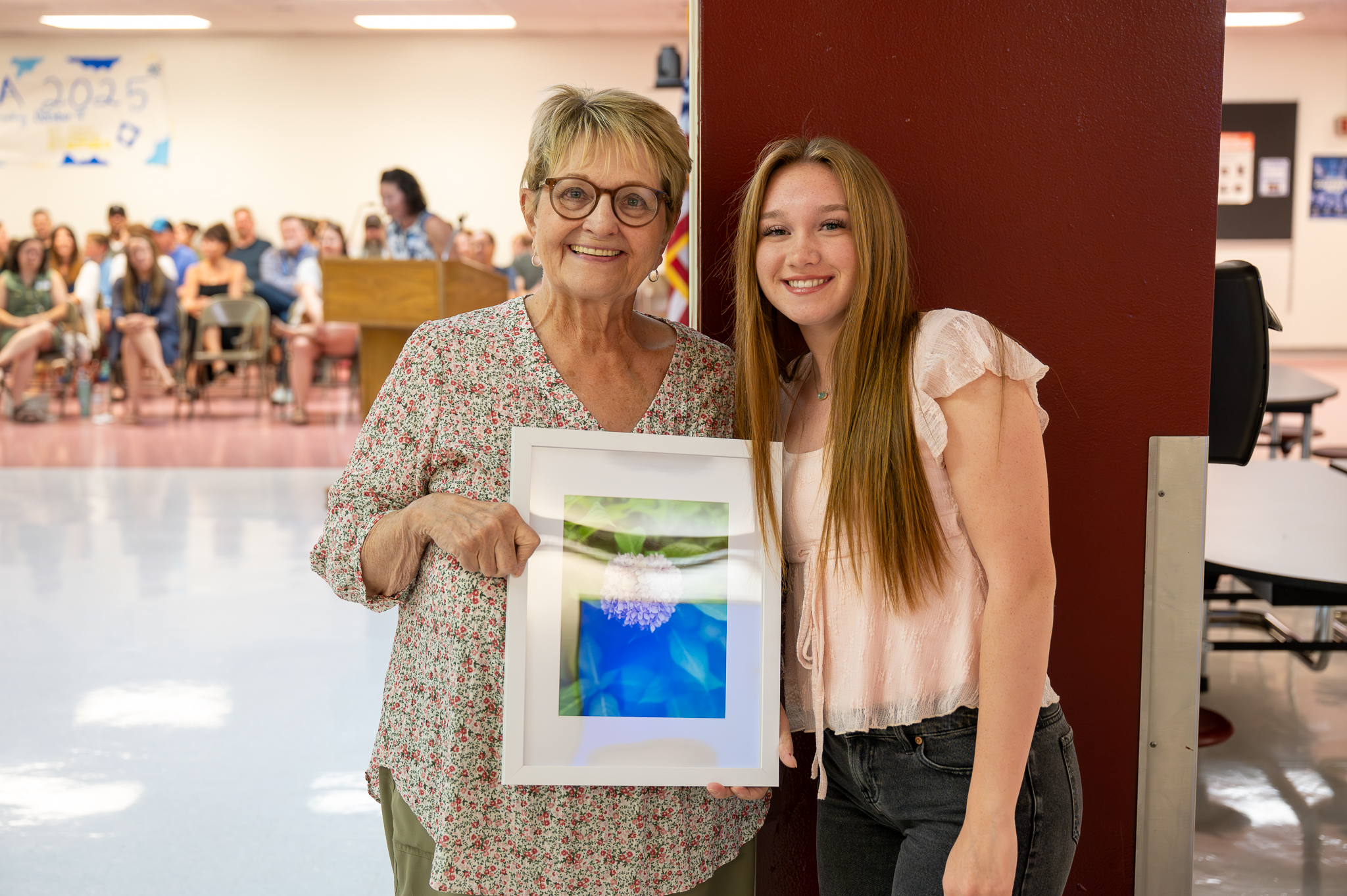 A board of education member standing proudly with a student, who gifted them artwork.